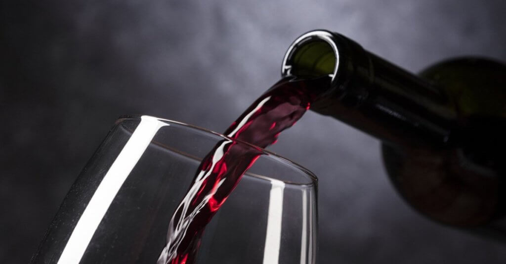 Rotwein wird aus einer Flasche in ein Glas gegossen